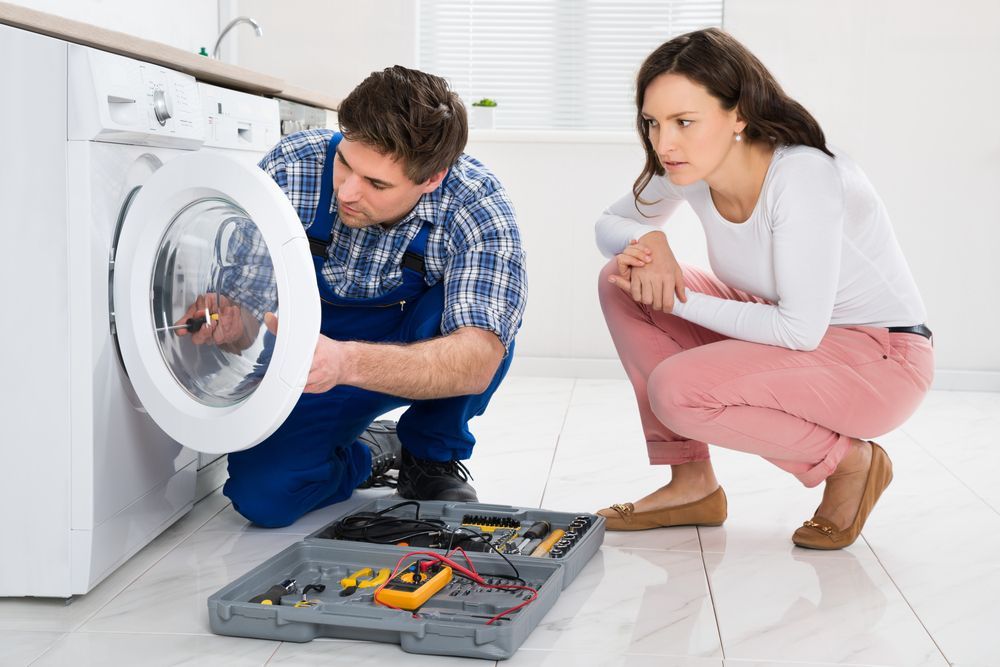 A woman watching the repairman fix her washer
