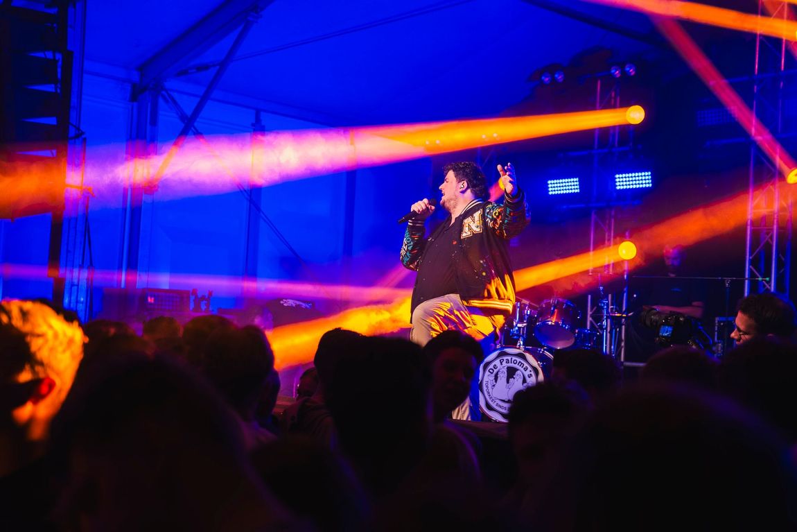 Een man zingt in een microfoon op een podium tijdens een concert.