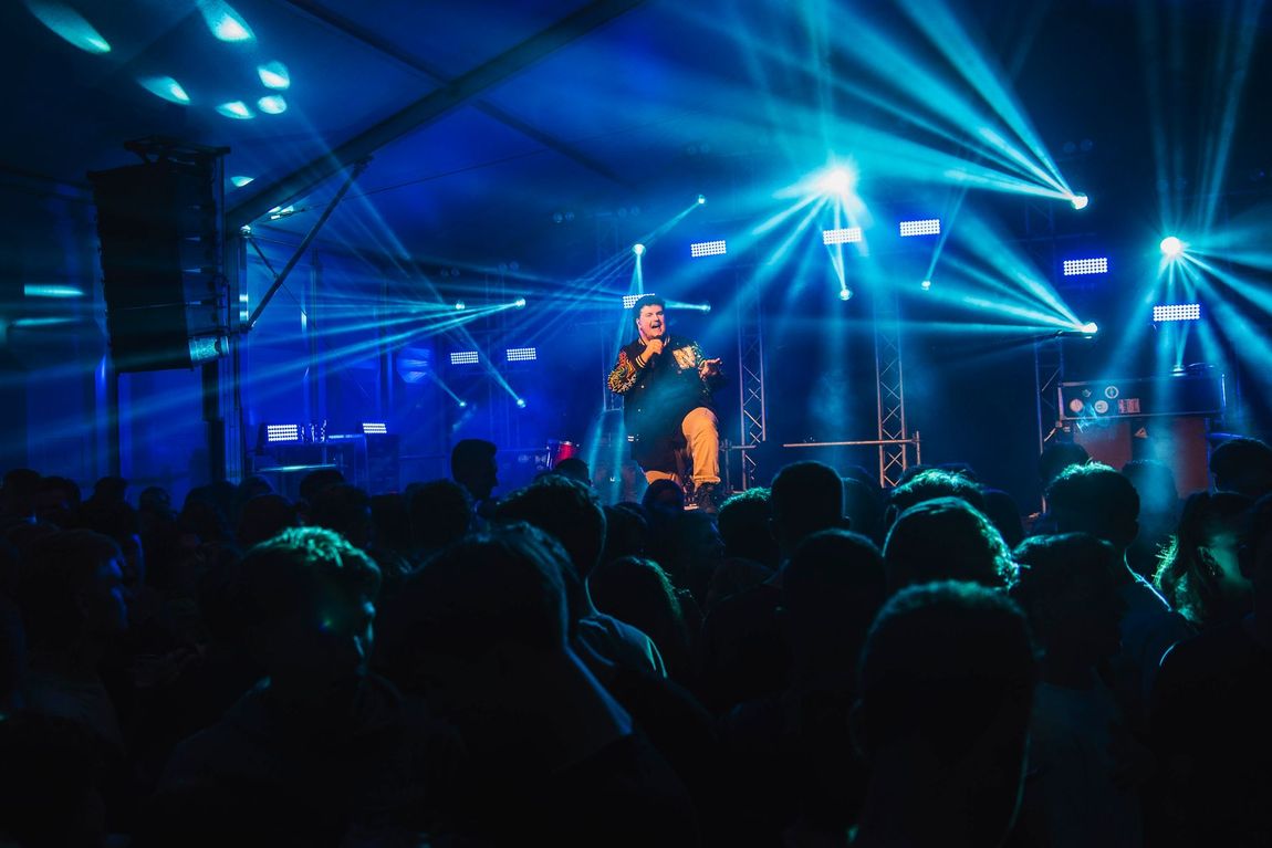 Een man zingt in een microfoon voor een menigte tijdens een concert.