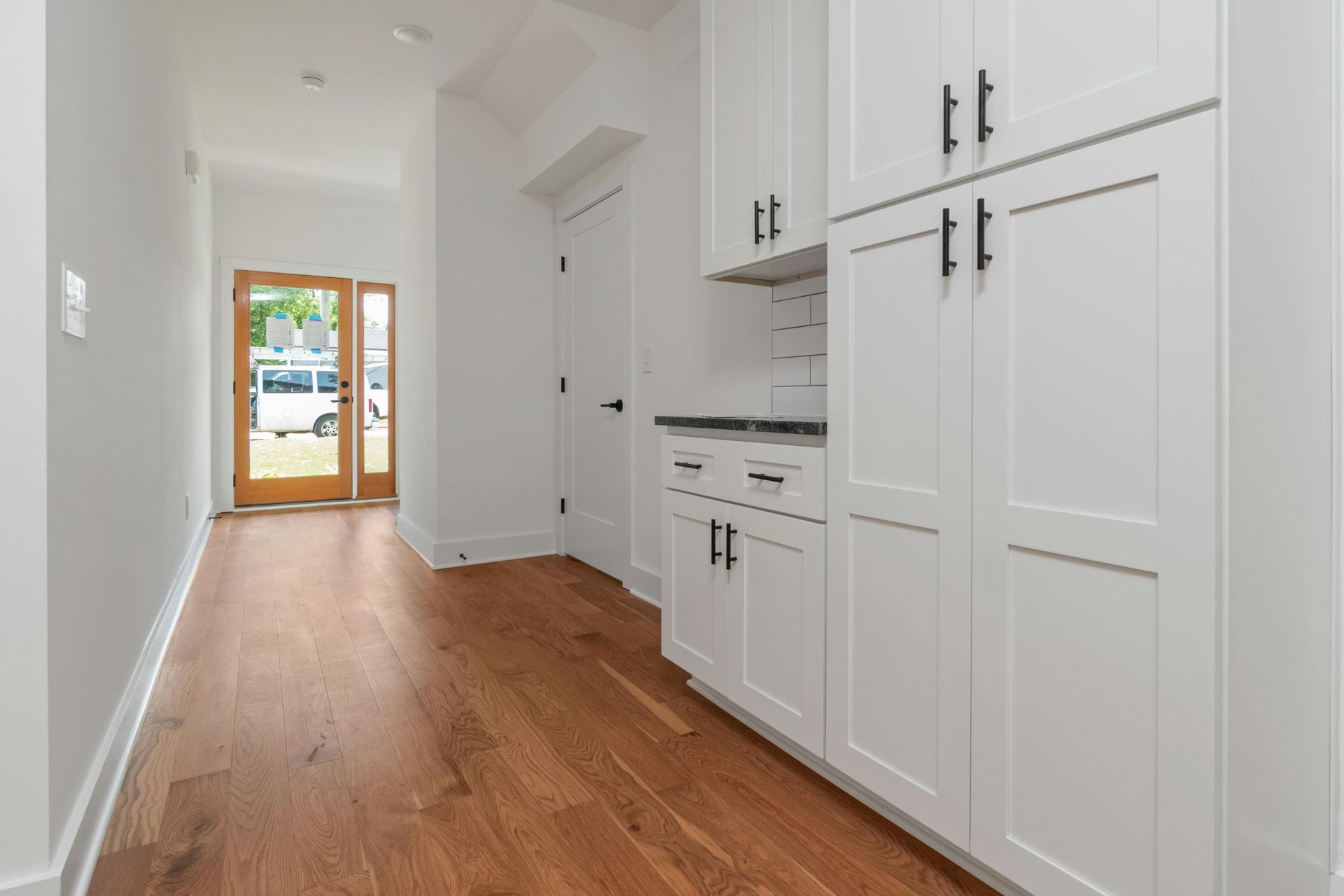 Hallway with hardwood floors and white cabinets, open doorway to exterior.