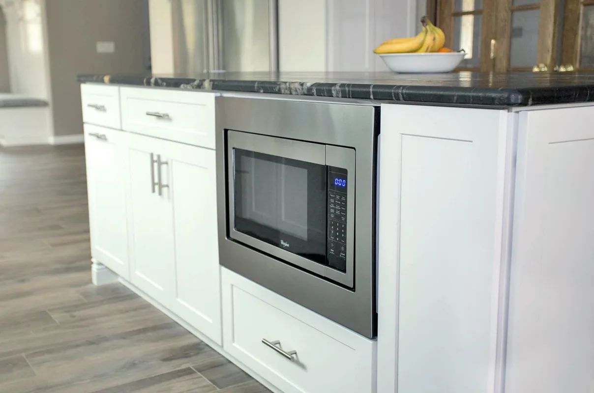 A kitchen with a microwave oven and a bowl of bananas on the counter.