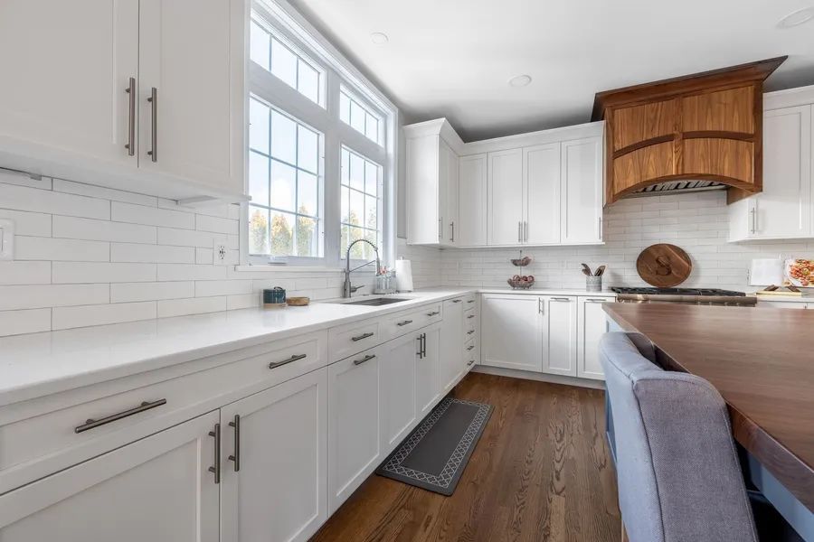 A kitchen with white cabinets, hardwood floors, and a large island.