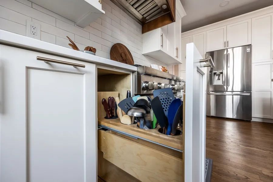 A kitchen with white cabinets and a drawer filled with utensils.