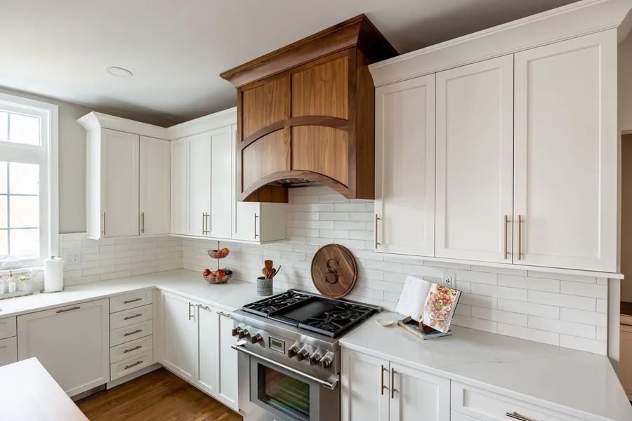 A kitchen with white cabinets, stainless steel appliances, and a wooden hood.