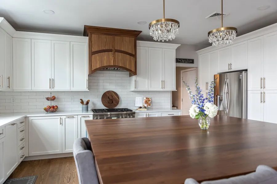 A kitchen with white cabinets and a wooden table with a vase of flowers on it.