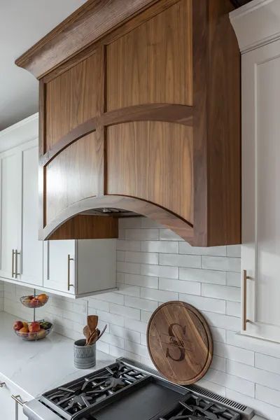 A kitchen with white cabinets and a wooden hood above the stove.