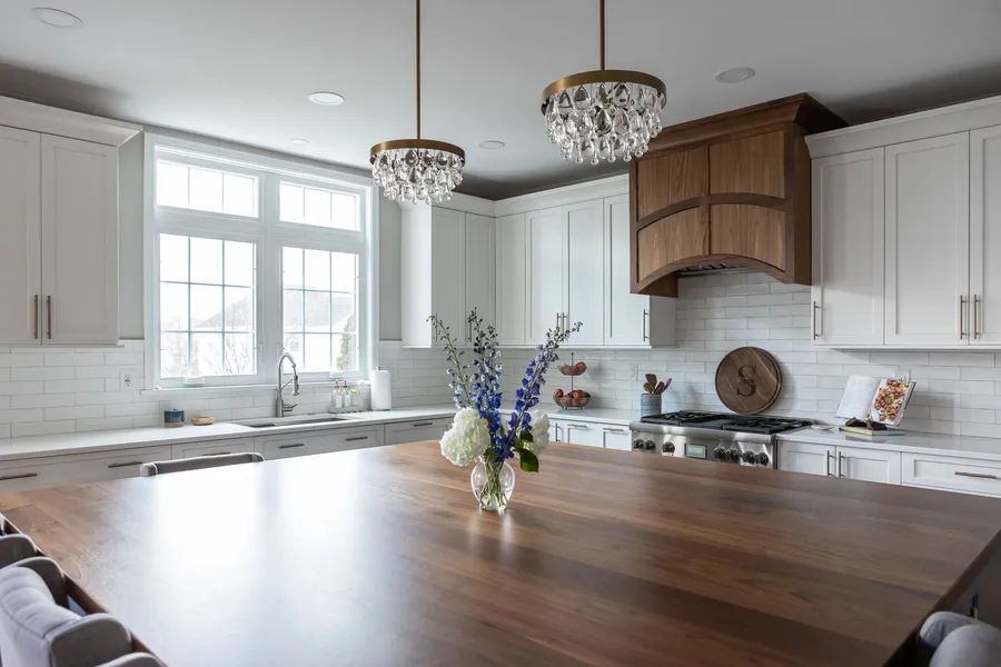A kitchen with white cabinets and a wooden table with a vase of flowers on it.