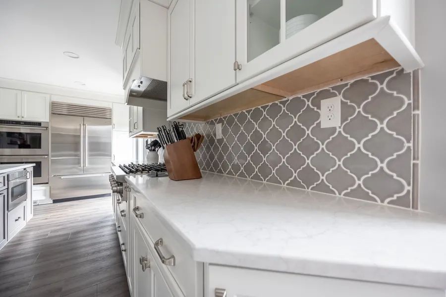 A kitchen with white cabinets and gray tiles on the back wall.