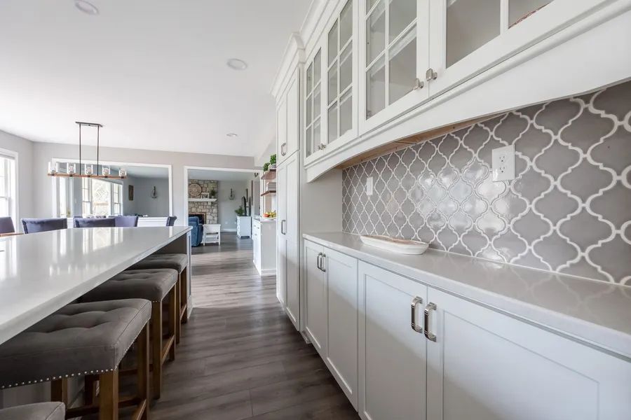 A kitchen with white cabinets and stools and a large island.