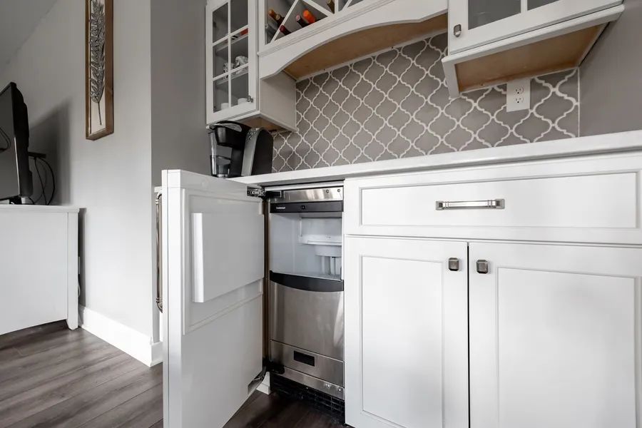 A kitchen with white cabinets and a stainless steel ice maker.