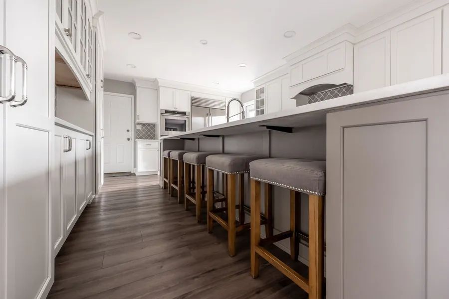 A kitchen with white cabinets and wooden floors and stools.