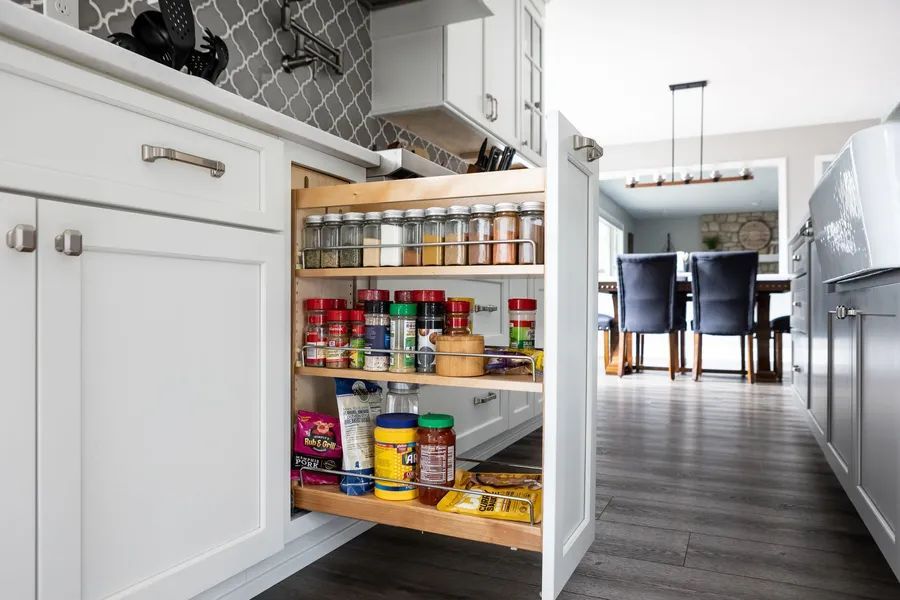 A kitchen with a pull out spice rack and a dining room in the background.