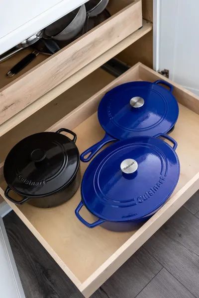Two blue pots and pans are in a wooden drawer.