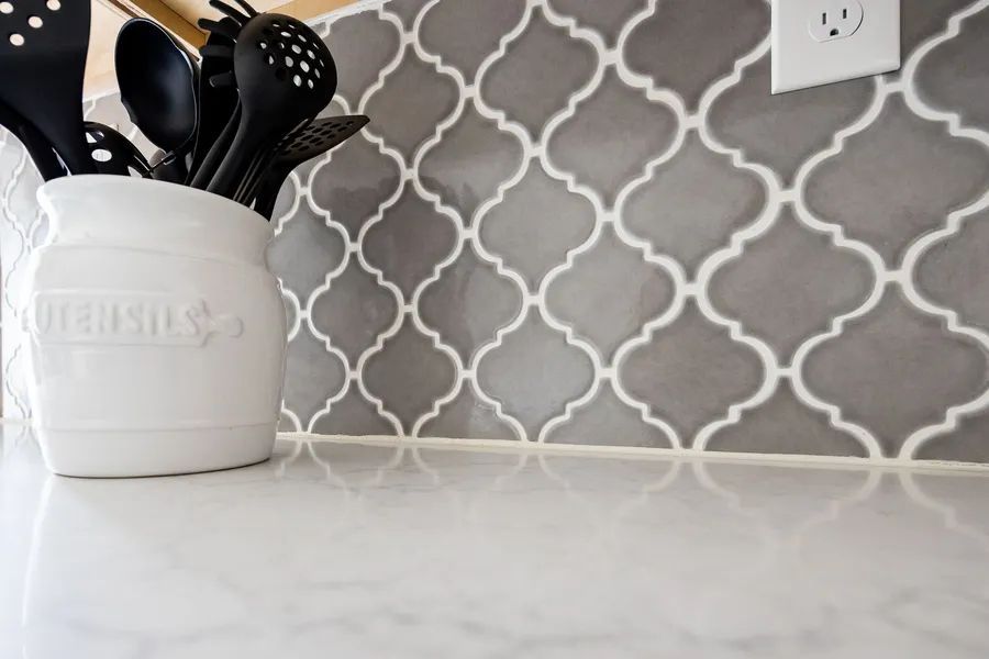 A white utensil holder is sitting on a counter next to a gray and white tile wall.