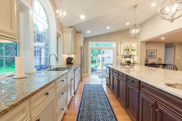 A kitchen with white cabinets , granite counter tops , and a blue rug.