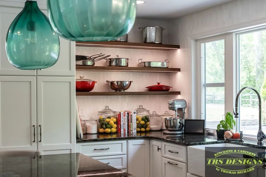 A kitchen with white cabinets, black counter tops, a sink, and shelves.