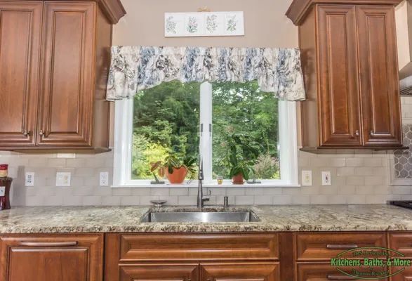 A kitchen with wooden cabinets , granite counter tops , a sink and a window.