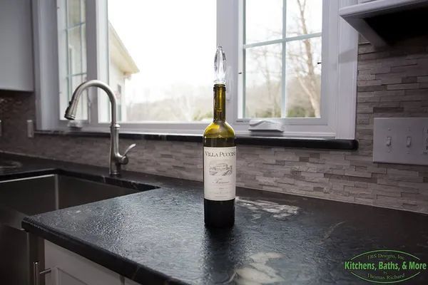 A bottle of wine is sitting on a kitchen counter next to a window.