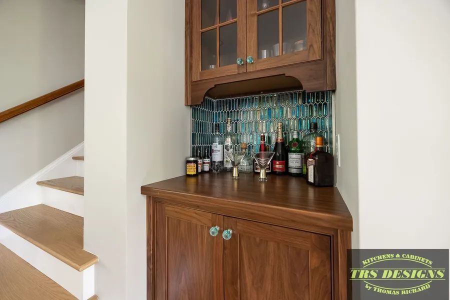 A bar with bottles and glasses on it in a room next to stairs.