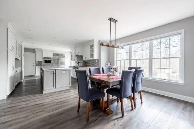 A dining room with a table and chairs and a kitchen in the background.