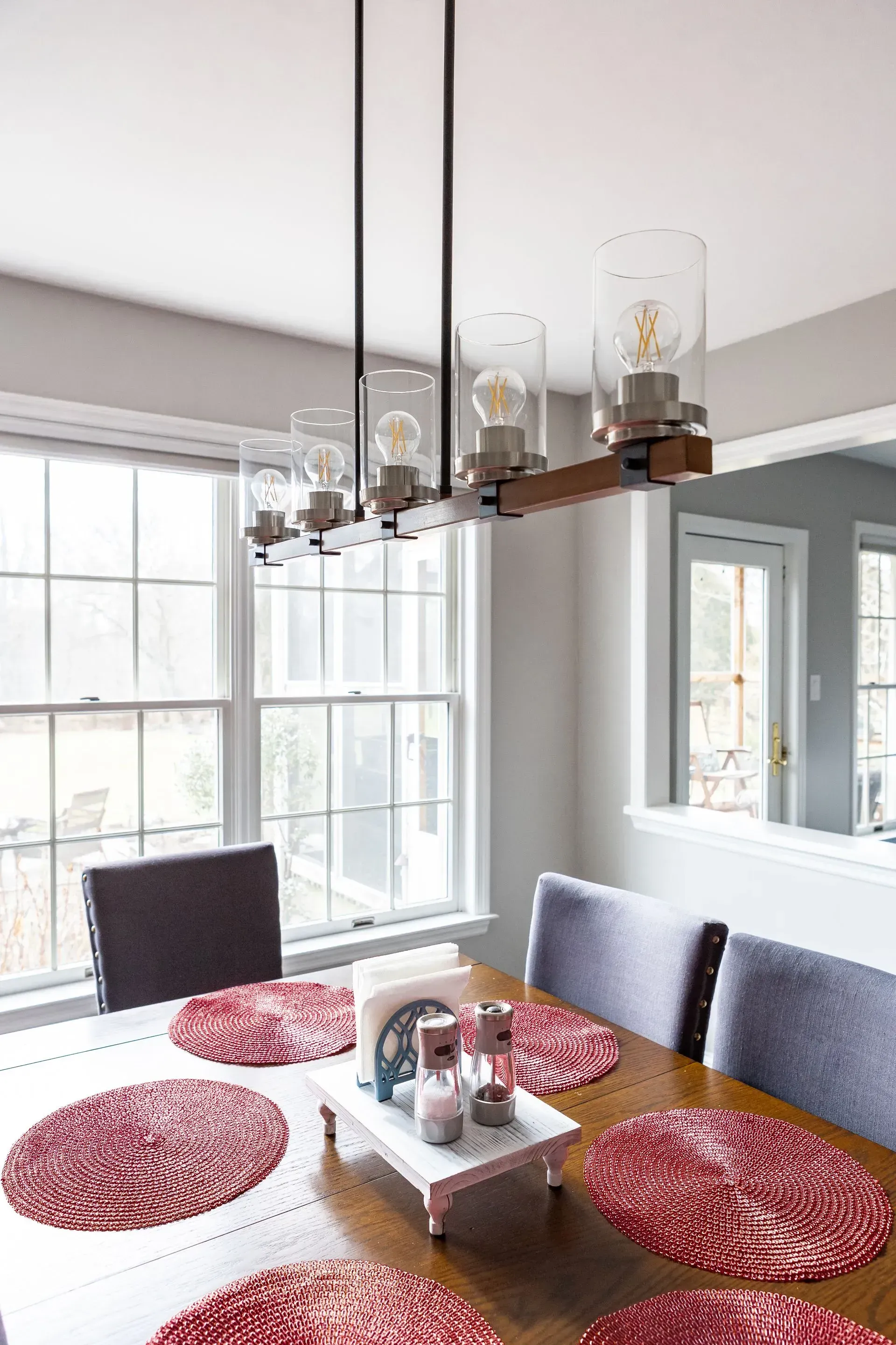 A dining room table with red place mats and a chandelier hanging from the ceiling.