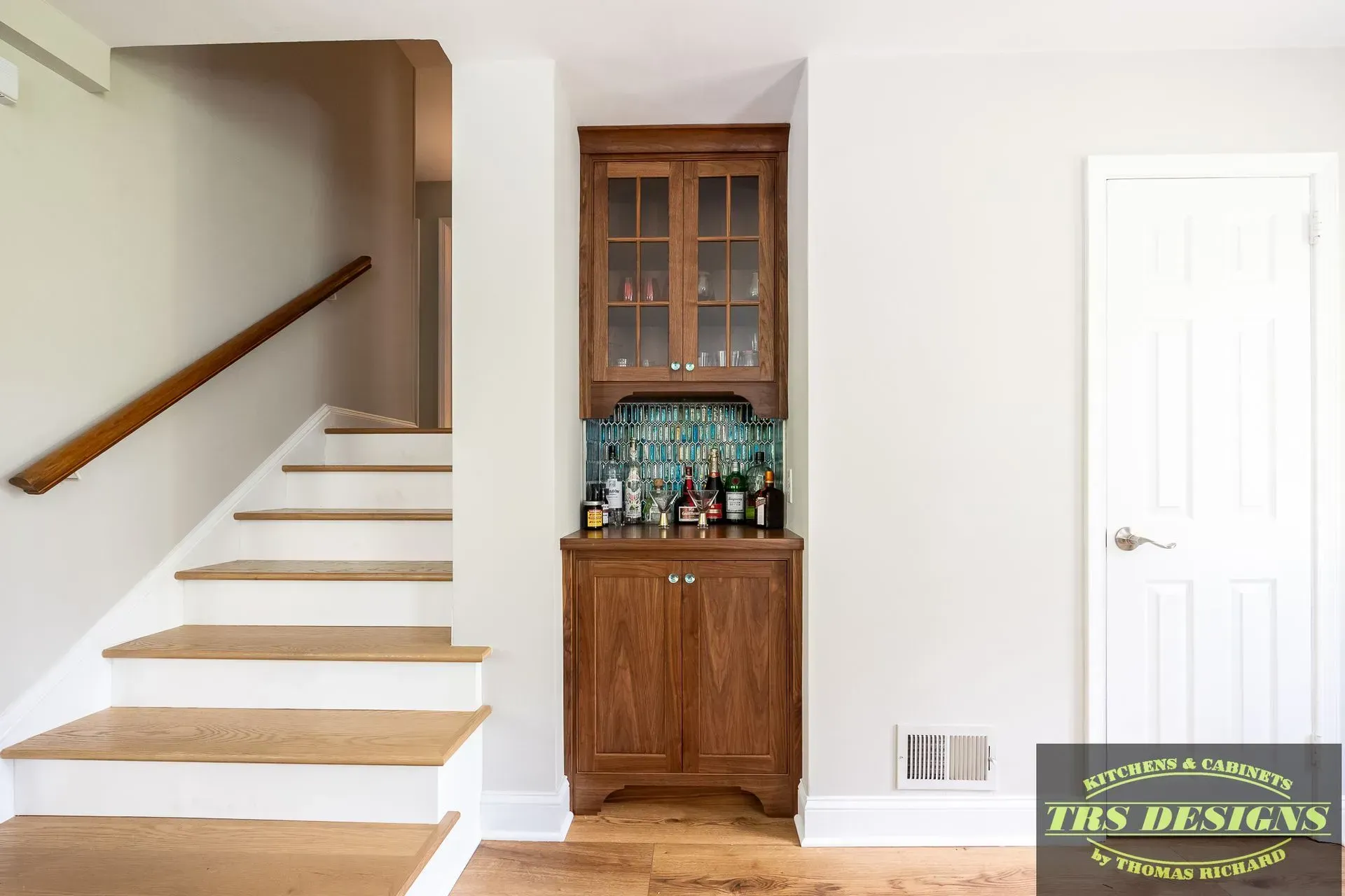 A room with stairs and a cabinet with bottles on it.