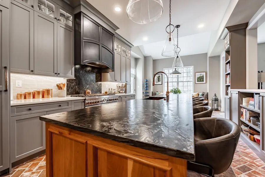 A kitchen with gray cabinets and a large island with a black counter top.