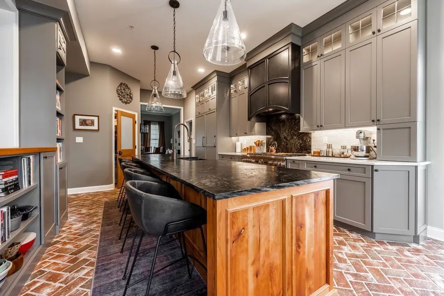 A kitchen with gray cabinets , black counter tops, and a large island.