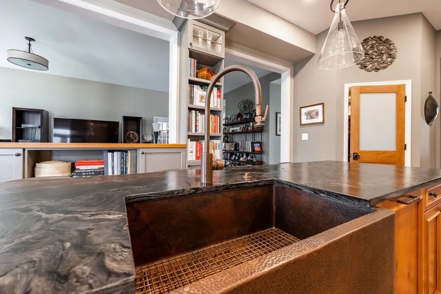 A kitchen with a copper sink and a black counter top.