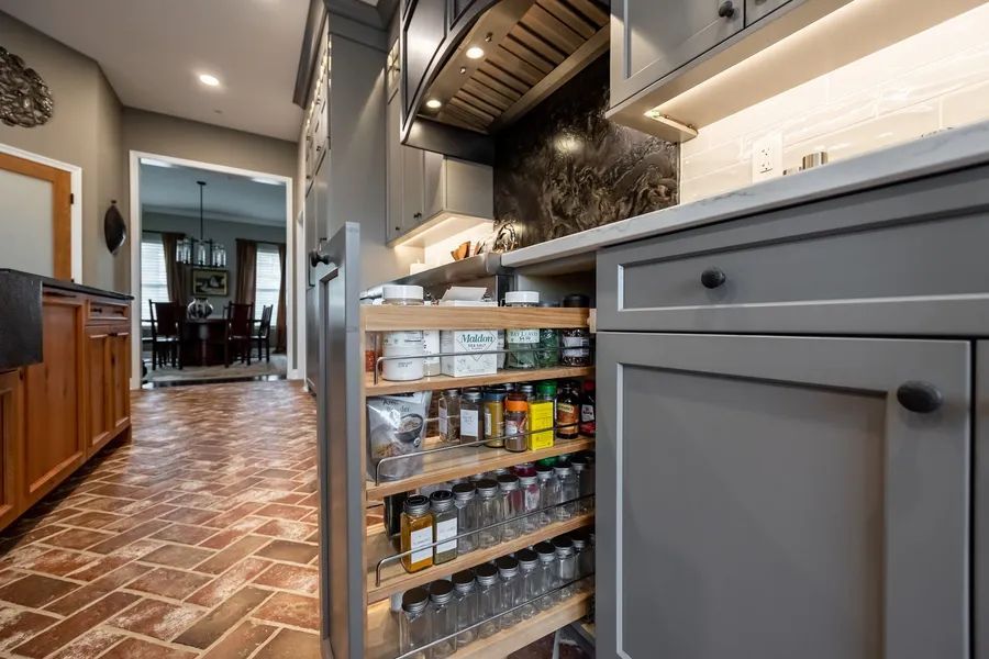 A kitchen with a pull out spice rack and a brick floor.