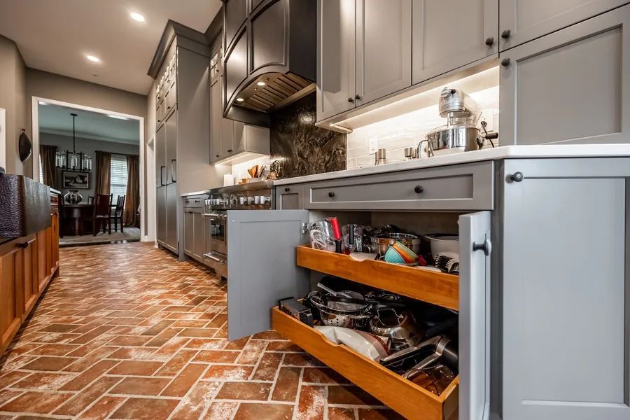 A kitchen with gray cabinets and wooden drawers filled with pots and pans.