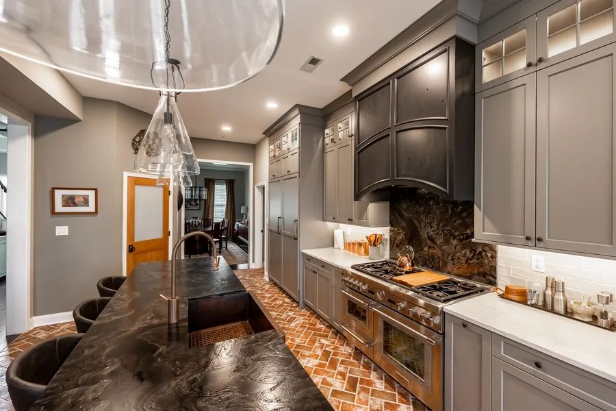 A kitchen with gray cabinets, black counter tops, stainless steel appliances and a large island.
