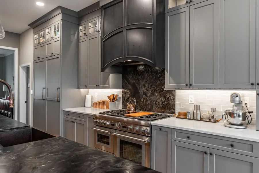 A kitchen with gray cabinets , black counter tops, a stove, and a sink.