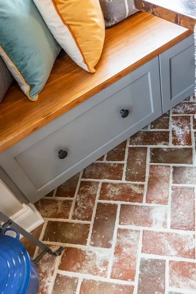 A wooden bench with drawers underneath it is sitting on a brick floor.