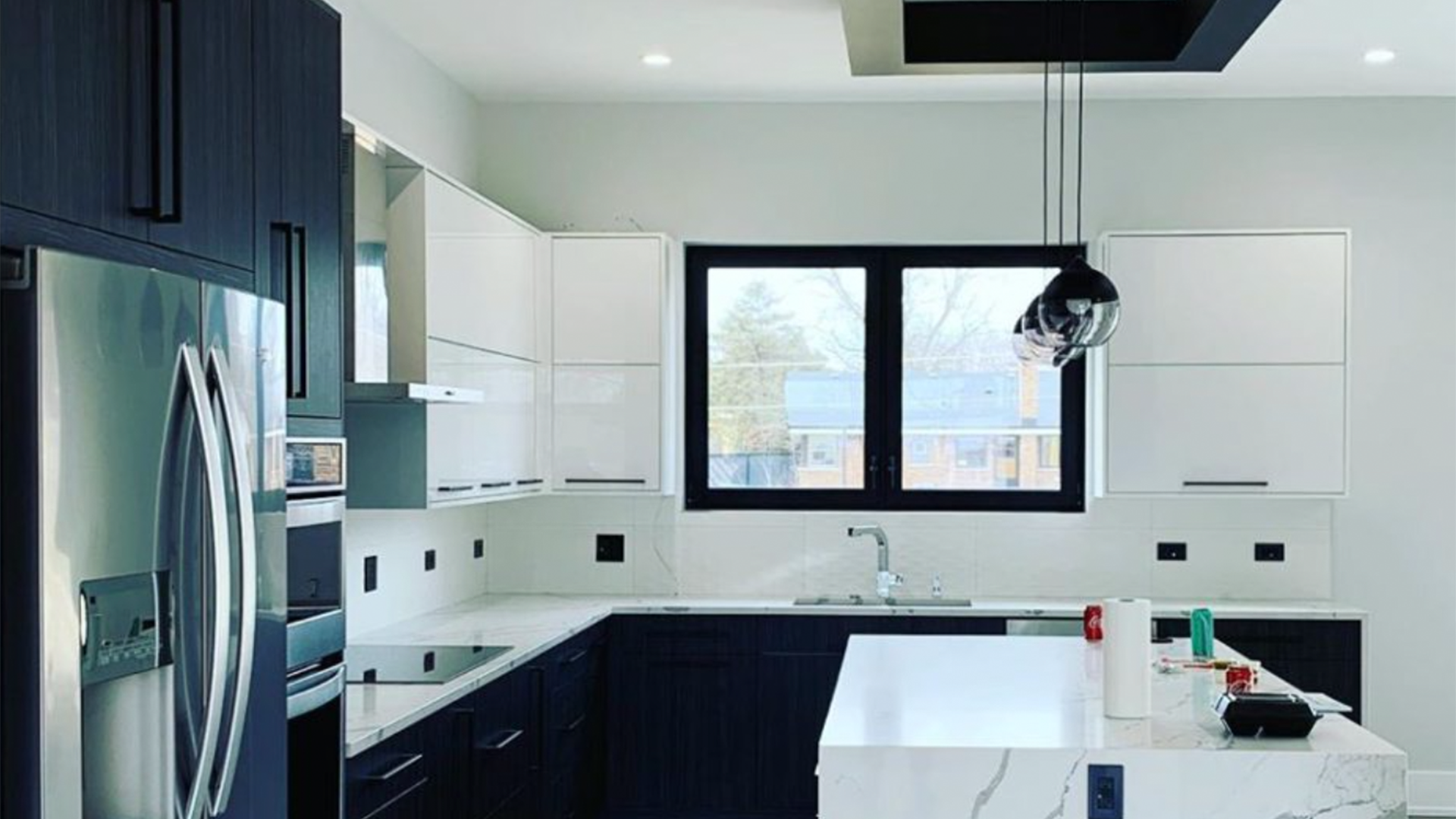 A kitchen with blue cabinets , white counter tops , stainless steel appliances and a large window.