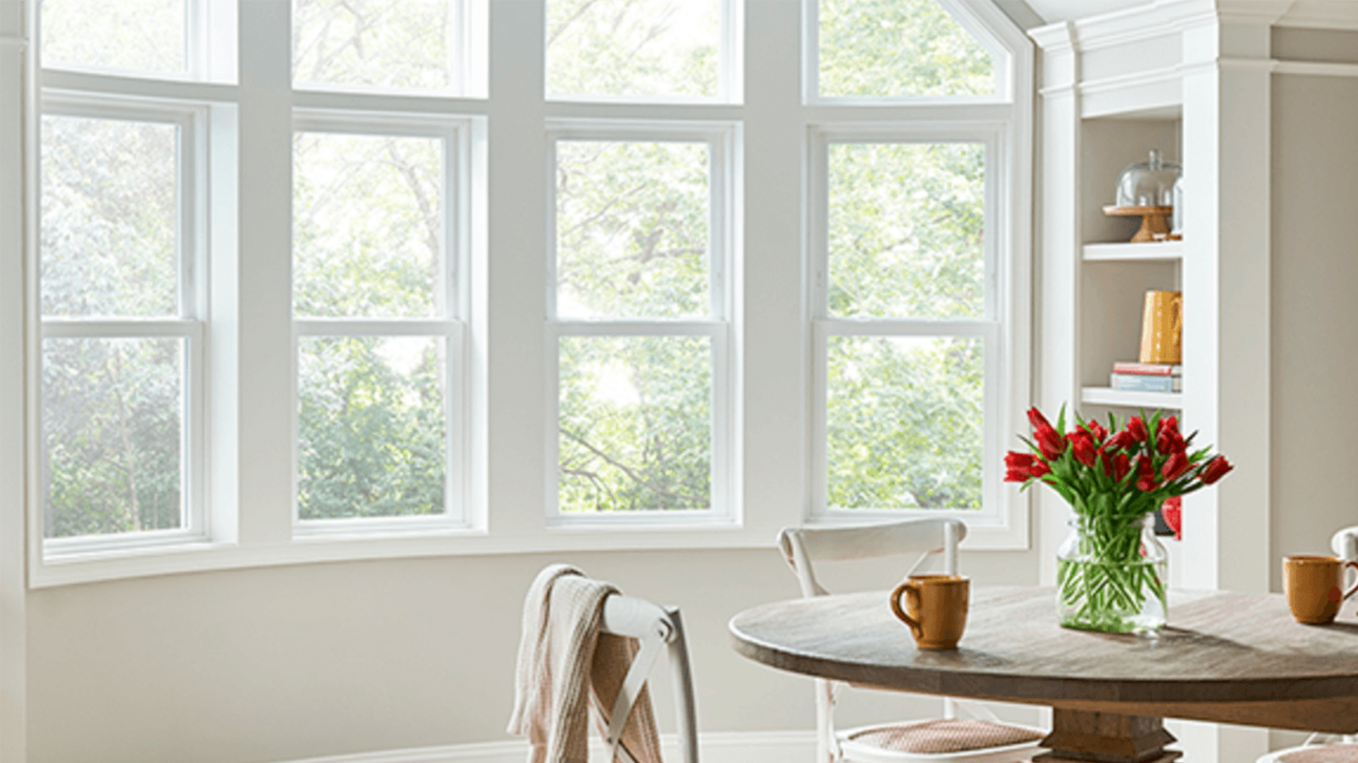 A dining room with a table and chairs and a vase of flowers on the table.