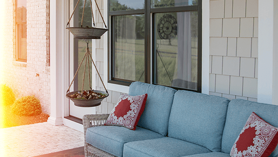 there is a couch on the porch of a house in front of sunrise windows.