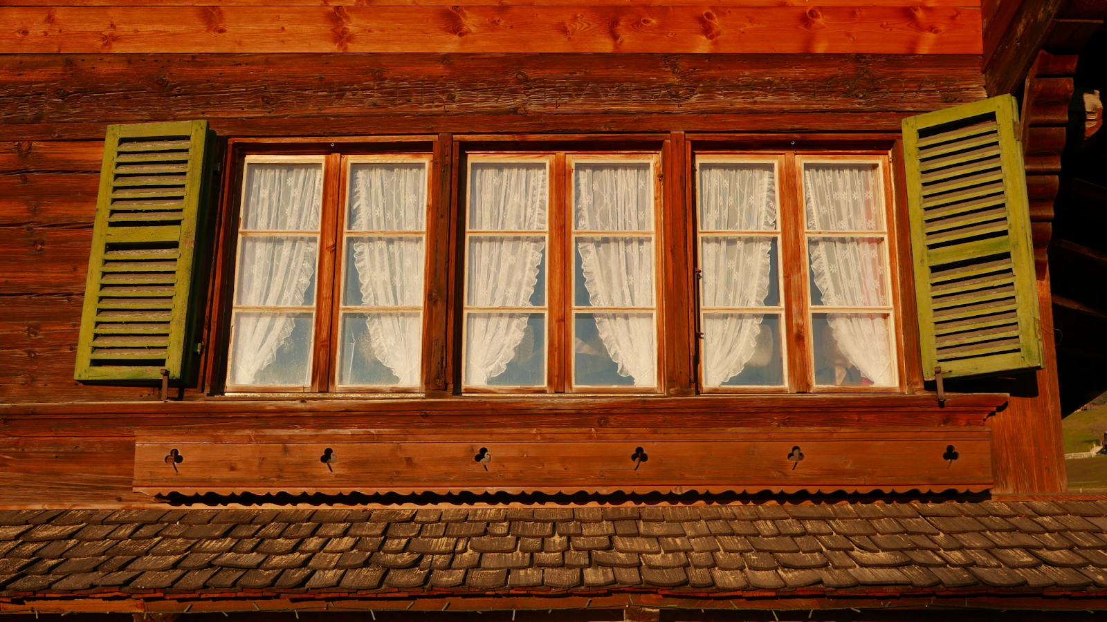 “Close-up of traditional wooden house window with lace curtains and green shutters on a rustic exter