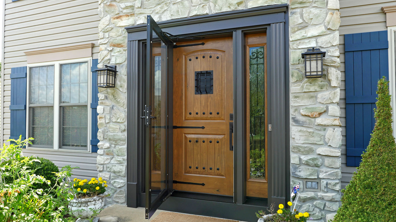 “Elegant wooden front entry door with decorative glass storm door set in a stone exterior home facad
