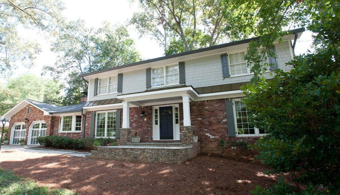 A large white brick house with a black door is surrounded by trees.