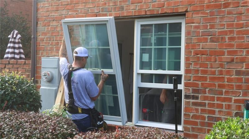 Technicians installing replacement windows in a brick home exterior during a residential window
