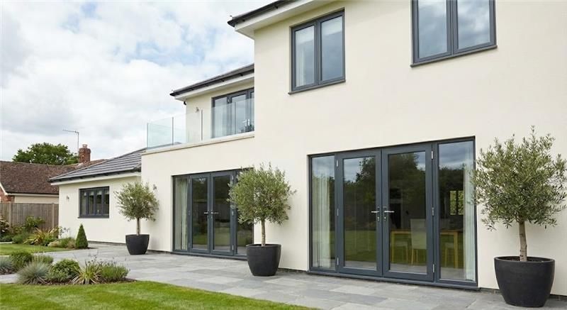 “Modern two-story house with large glass windows and sliding doors opening to a landscaped backyard 