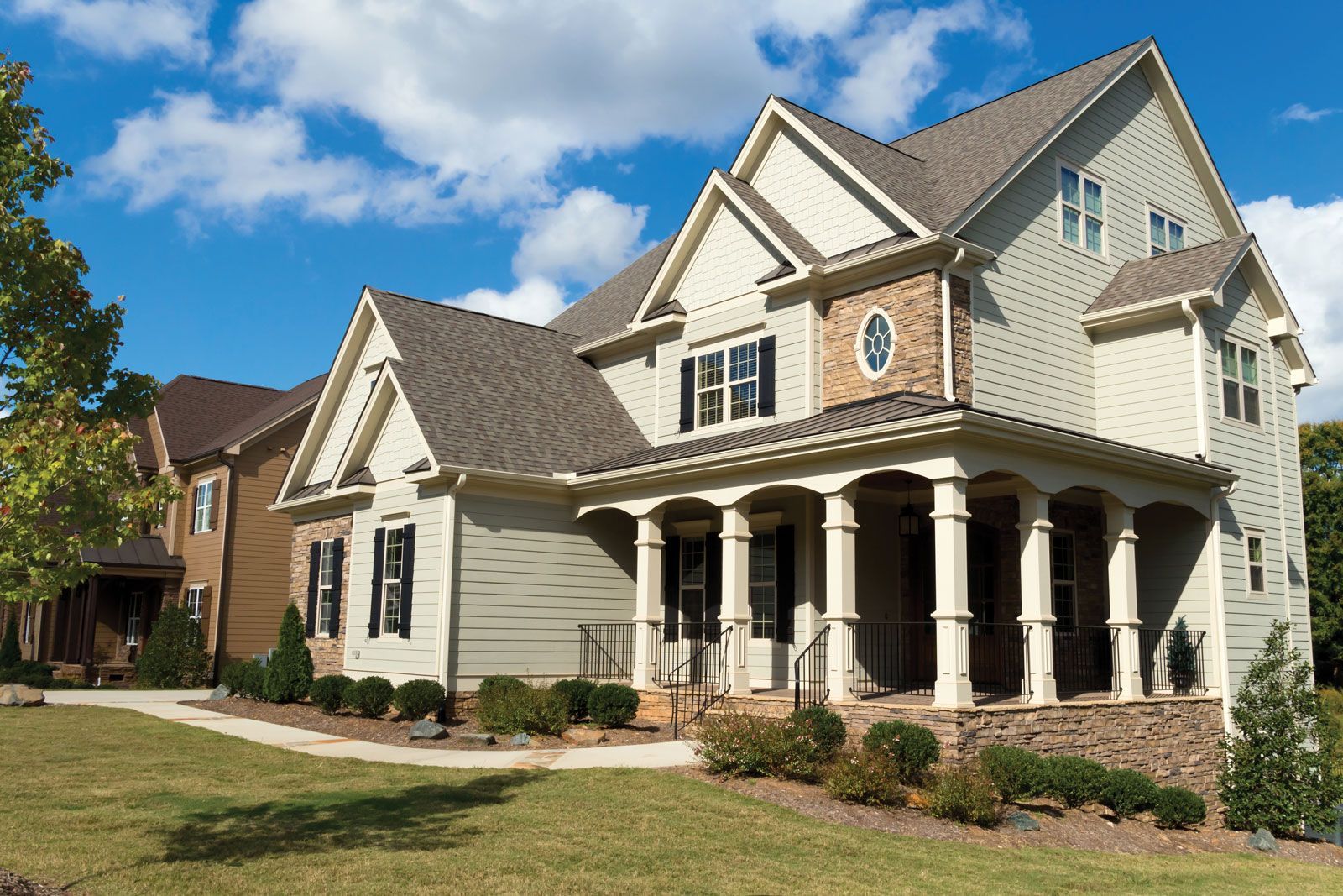 A large house with a large porch is sitting on top of a lush green hillside.