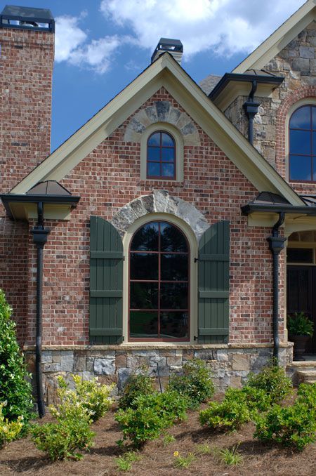 A brick house with arched windows and green shutters