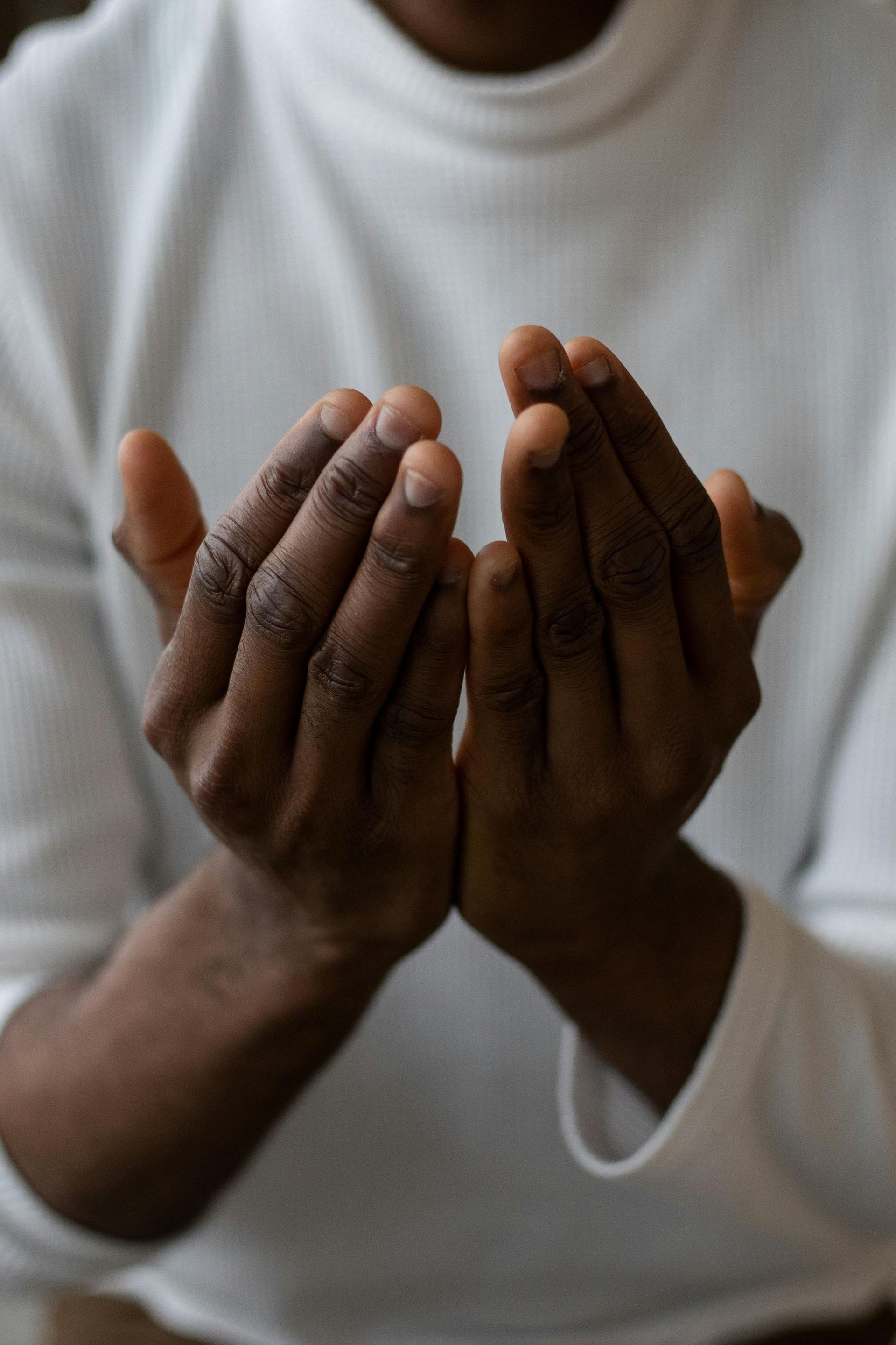 Person with dark skin holding hands open, palms up, wearing a white long-sleeved shirt.