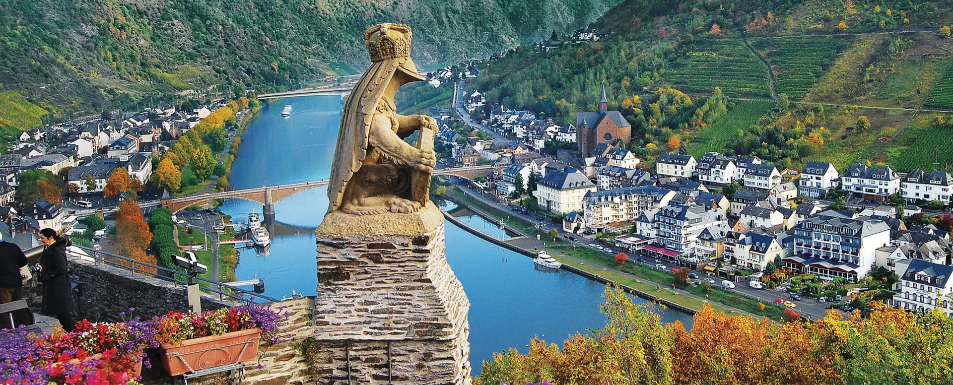 A statue of a man sitting on top of a stone tower overlooking a river and a city.