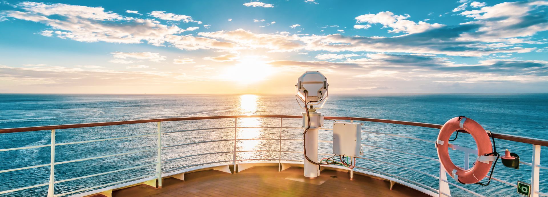 The sun is setting over the ocean from the deck of a cruise ship.