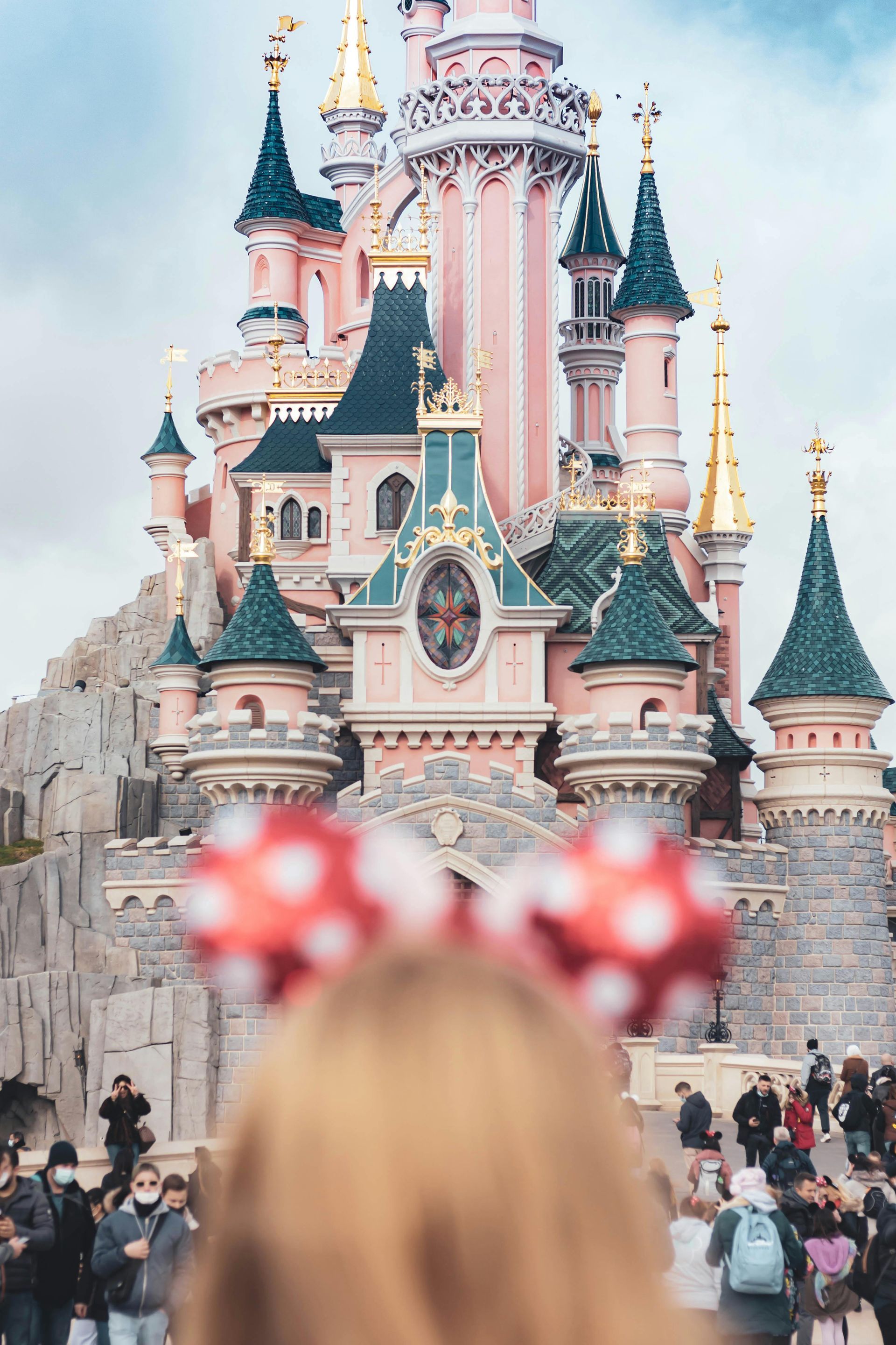 A woman wearing minnie mouse ears is standing in front of a castle.