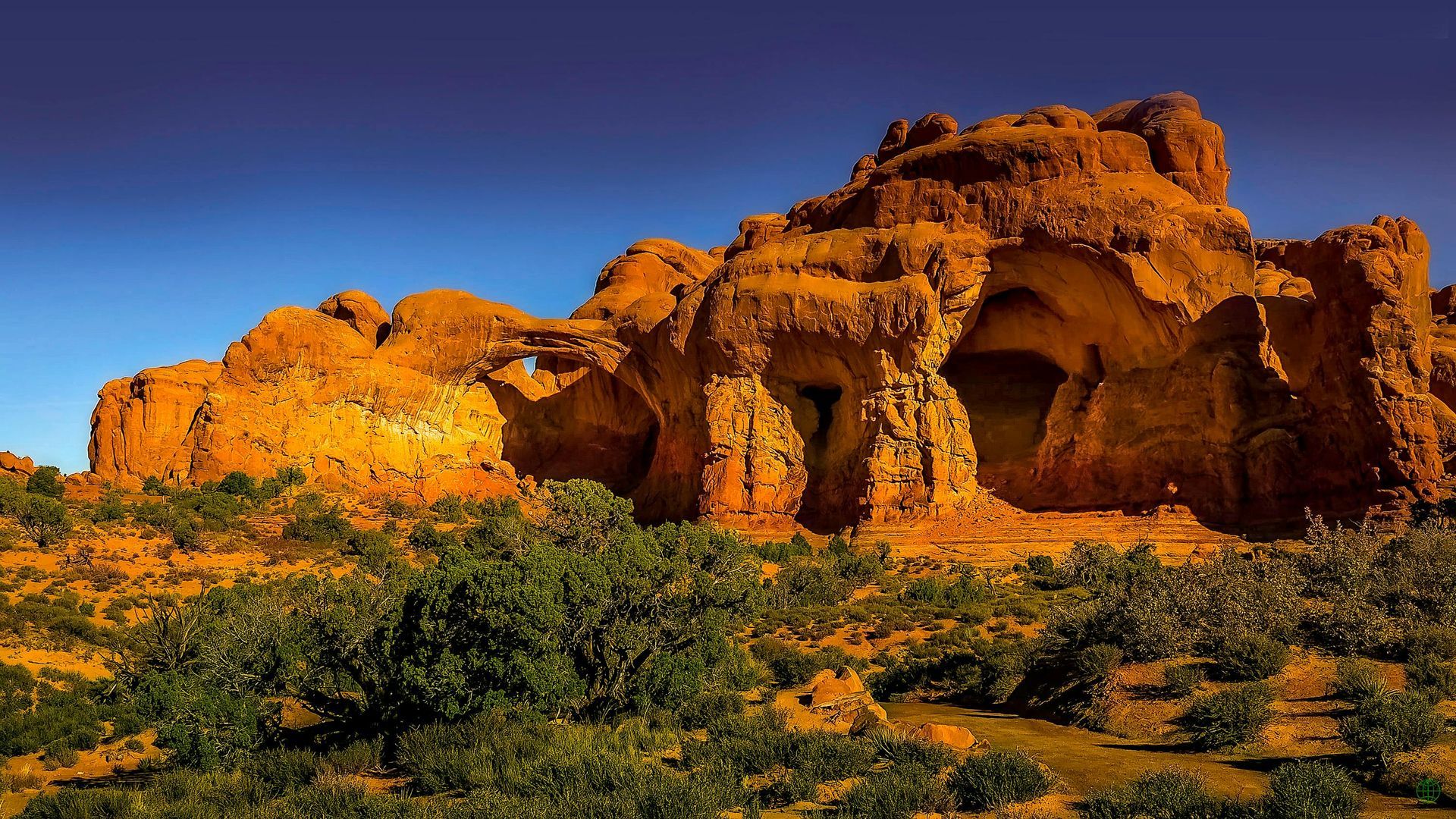 A large rock formation in the middle of a desert surrounded by trees.