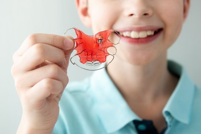 Boy holding a red dental retainer, smiling.